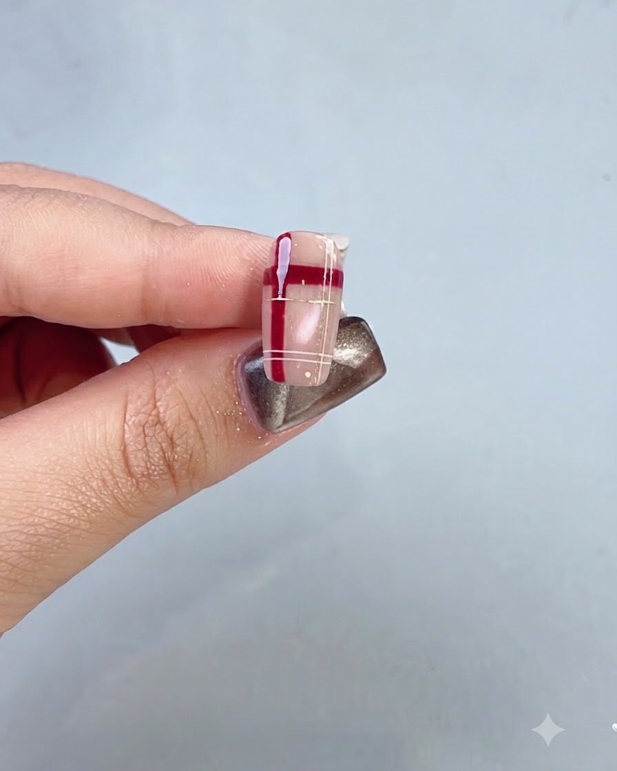 Primer plano de una uña terminada que presenta una celosía de cristal rojo y un diseño a cuadros.