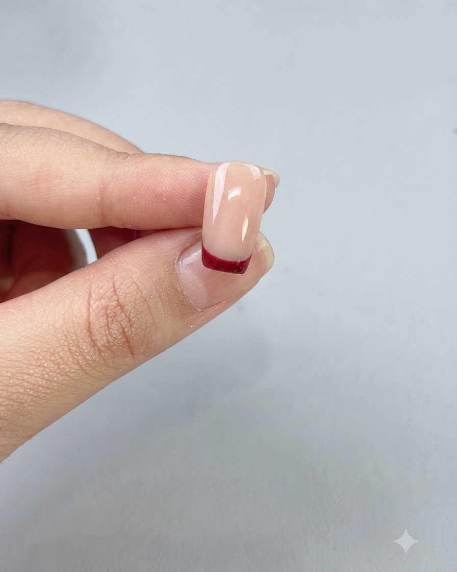 Una uña terminada con una limpia punta francesa en rojo sangre de buey sellada bajo un top coat brillante.