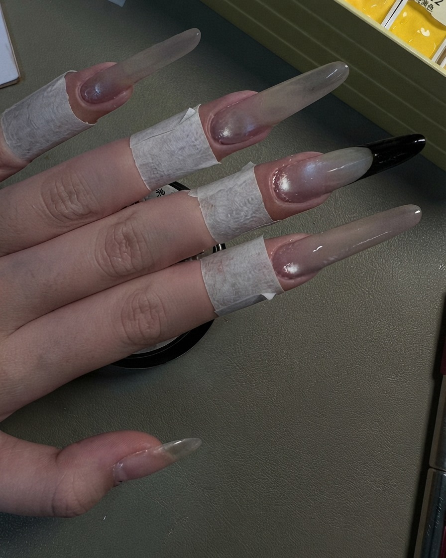 Una mano mostrando cuatro uñas stiletto largas terminadas con un aspecto brillante de ojo de gato gris perlado.