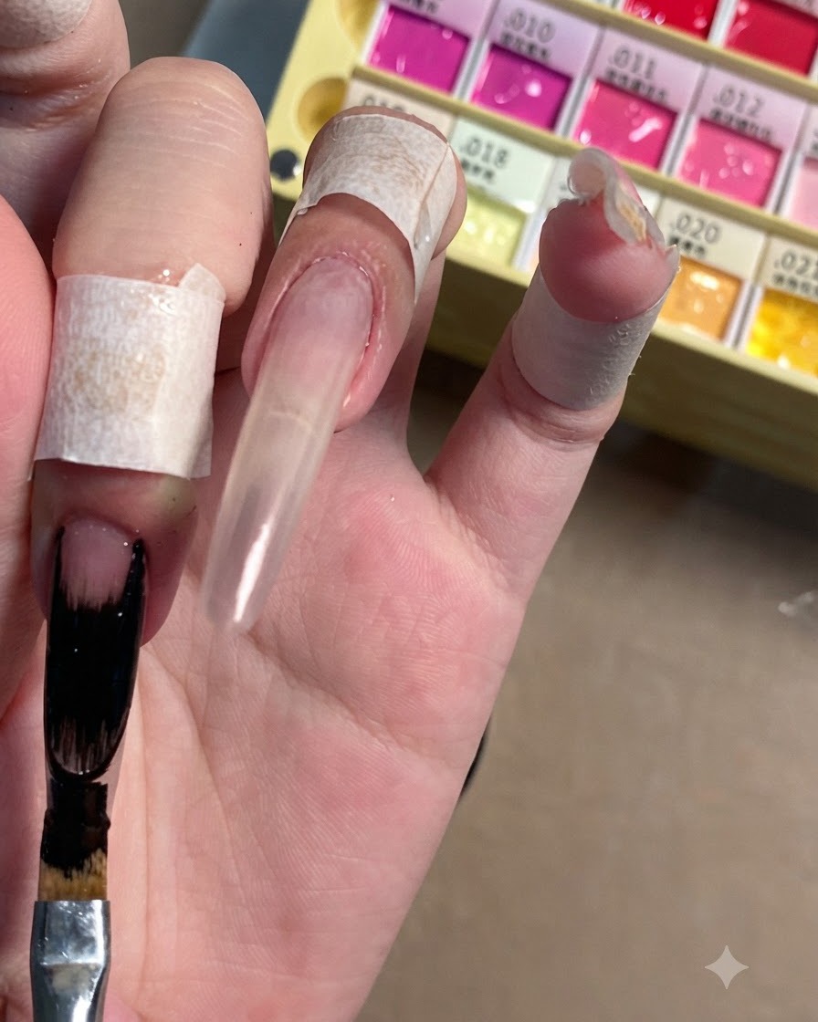 Un pincel plano para nail art aplicando esmalte en gel negro opaco en la punta alargada de una uña stiletto transparente.
