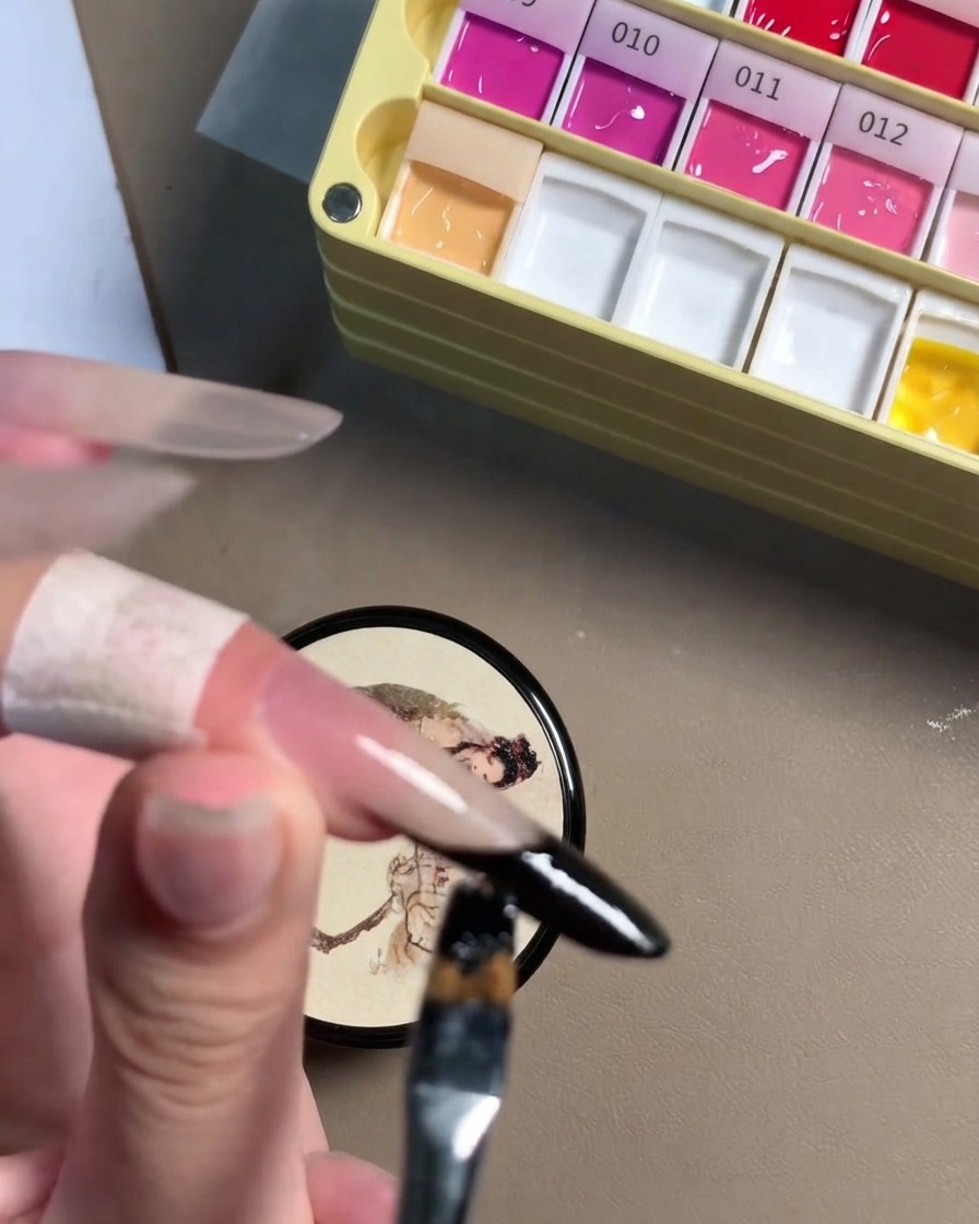 Una vista de cerca de un pincel de detalle perfeccionando la línea de gel negro en el borde de una uña stiletto.