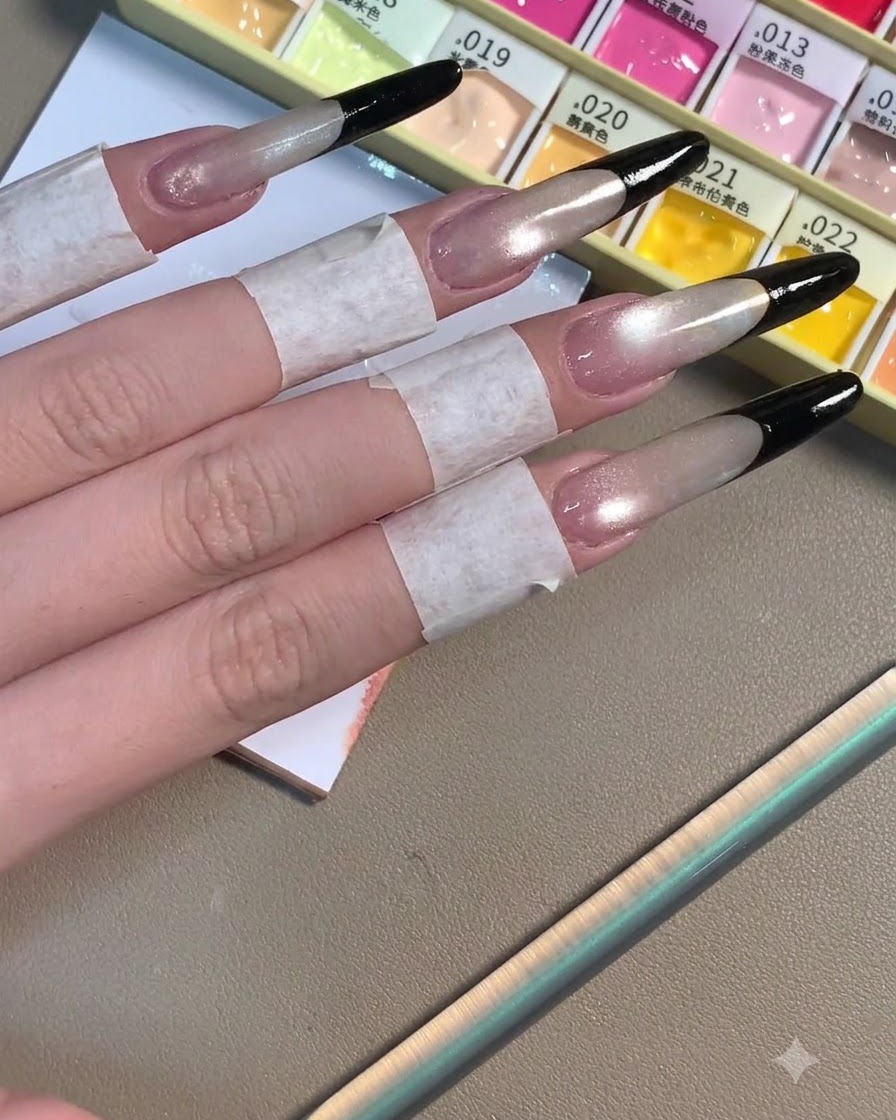 Cuatro uñas stiletto largas que muestran puntas francesas negras profundas y completadas sobre una base brillante en tono gris.