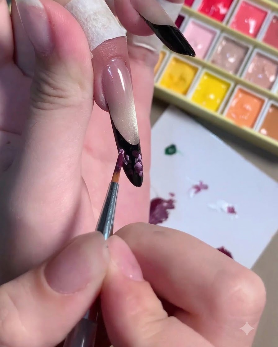 Un pincel fino aplicando trazos de realce en rosa claro sobre el arte floral en tono ciruela oscuro.