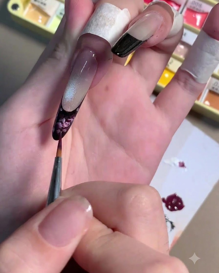 Un pincel delineador fino aplicando trazos de gel rosa claro sobre una base de rosa ciruela oscura en una uña.