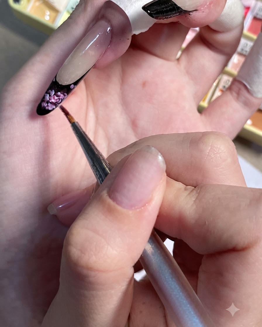 Un pincel de detalle colocando pequeños puntos de realce en rosa claro sobre la punta francesa negra de una uña pintada.