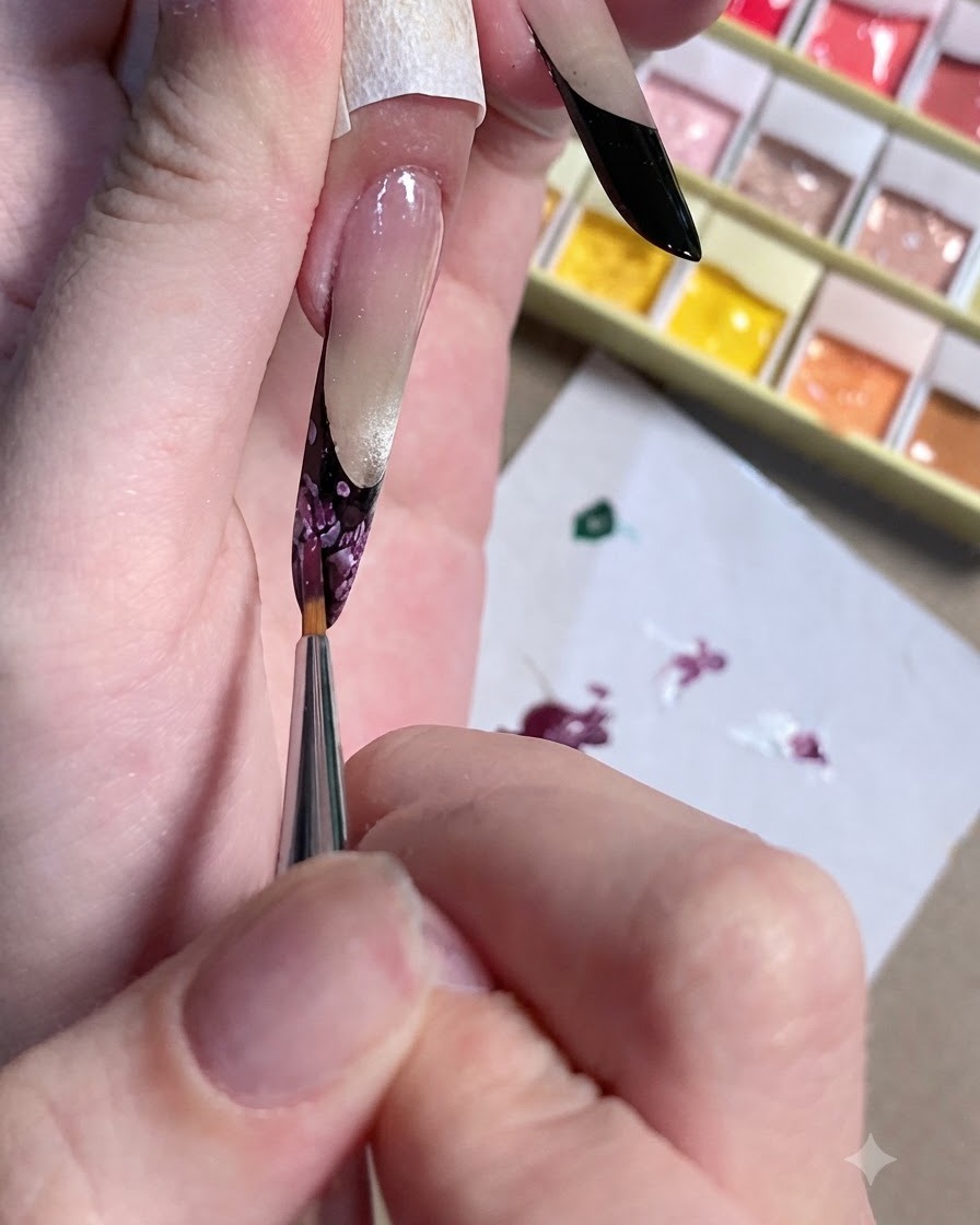 Un primer plano de un pincel de detalle refinando el centro oscuro de un diseño de uña floral.
