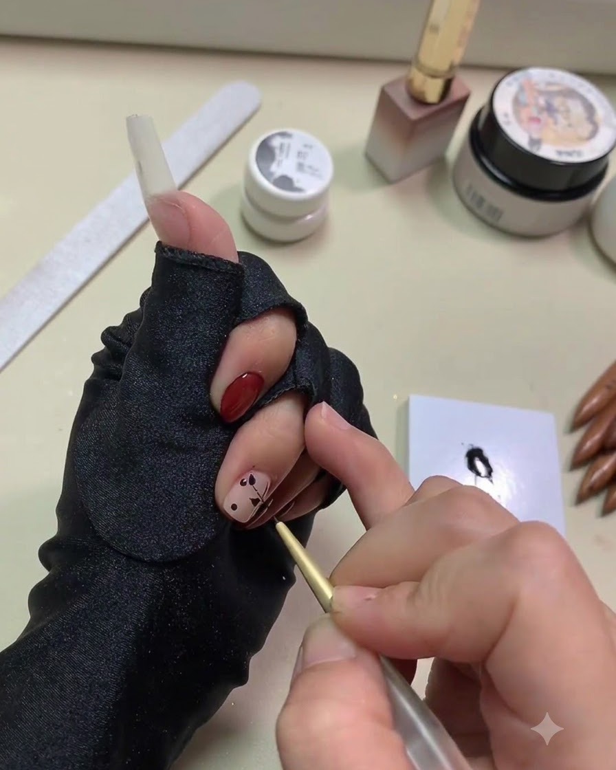 Primer plano de una mano usando un pincel liner dorado fino para arrastrar gel negro en forma de hojas desde puntos sobre una base nude.