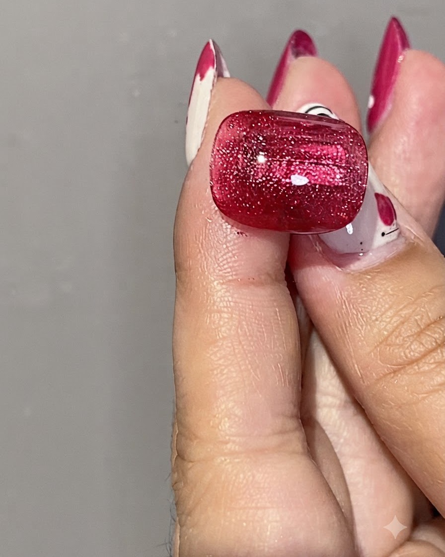 Un primer plano de una mano sosteniendo un imán cilíndrico plateado cerca de una uña de gel rojo brillante de ojo de gato para dar forma al brillo magnético.
