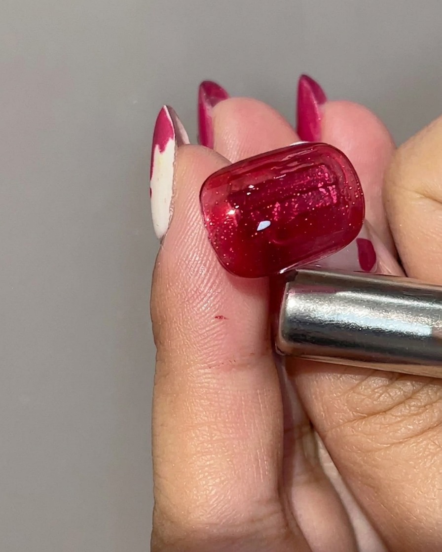 Una vista de cerca de una uña de gel rojo de ojo de gato curada que muestra un color base carmesí profundo con una franja de luz magnética concentrada.