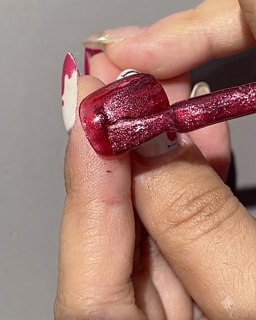 Un pincel aplicando una segunda capa de esmalte en gel rojo brillante de ojo de gato sobre una uña ya pintada de rojo.