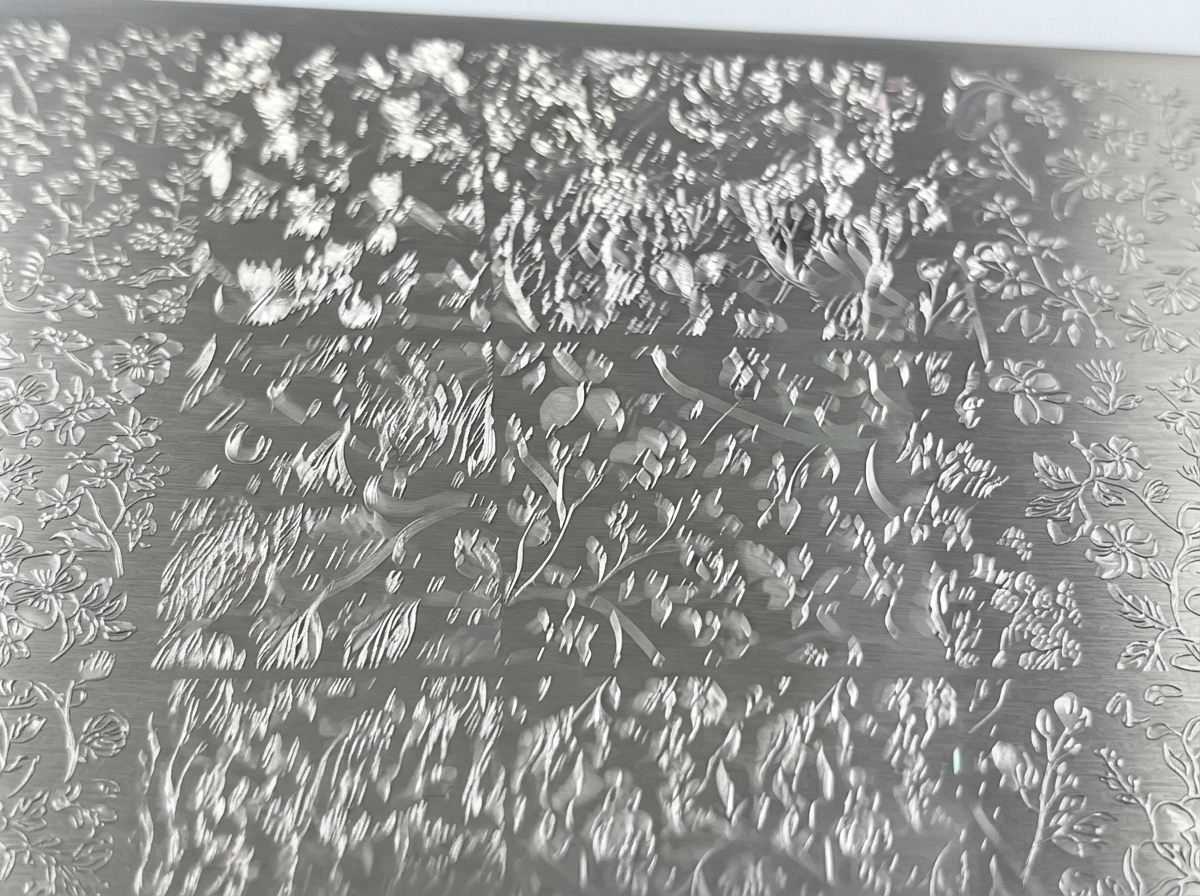 Una vista de cerca de una placa de metal para estampado grabada con diseños florales detallados.