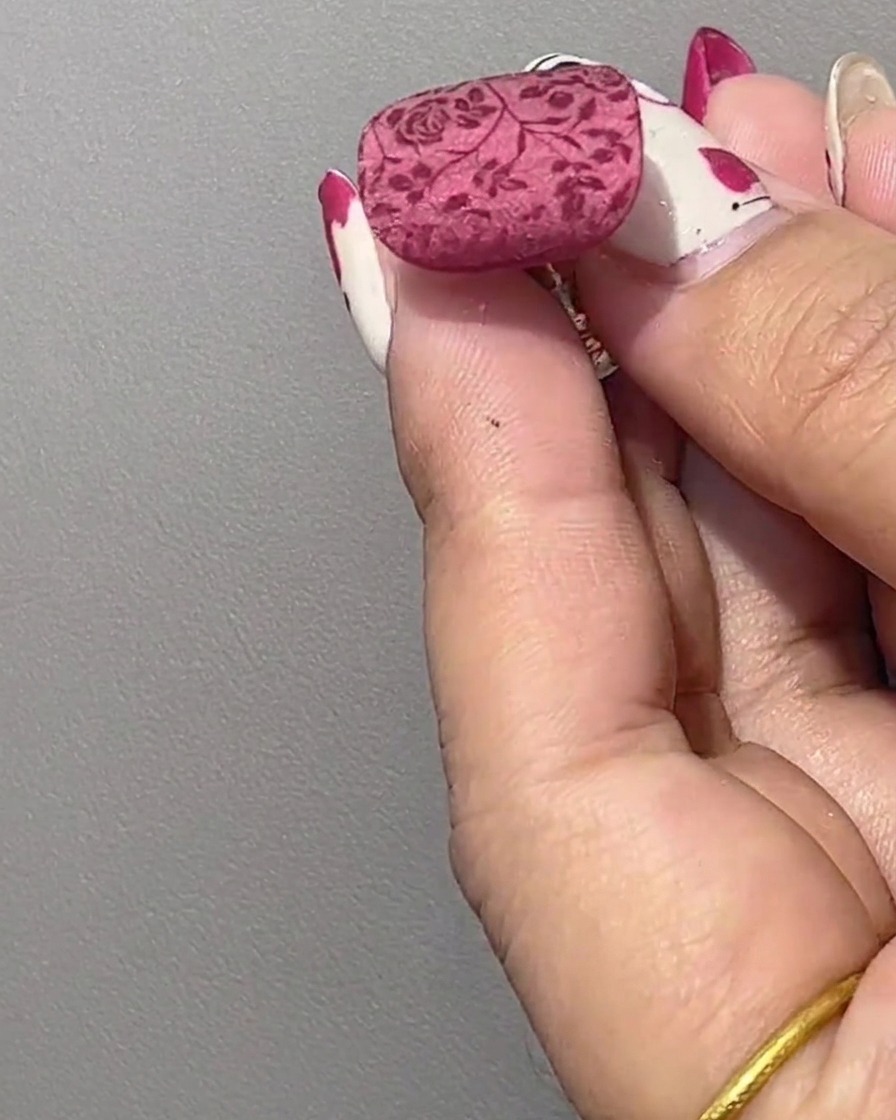 Primer plano de una uña arreglada que muestra un patrón floral rojo transferido sobre una base brillante sin curar.