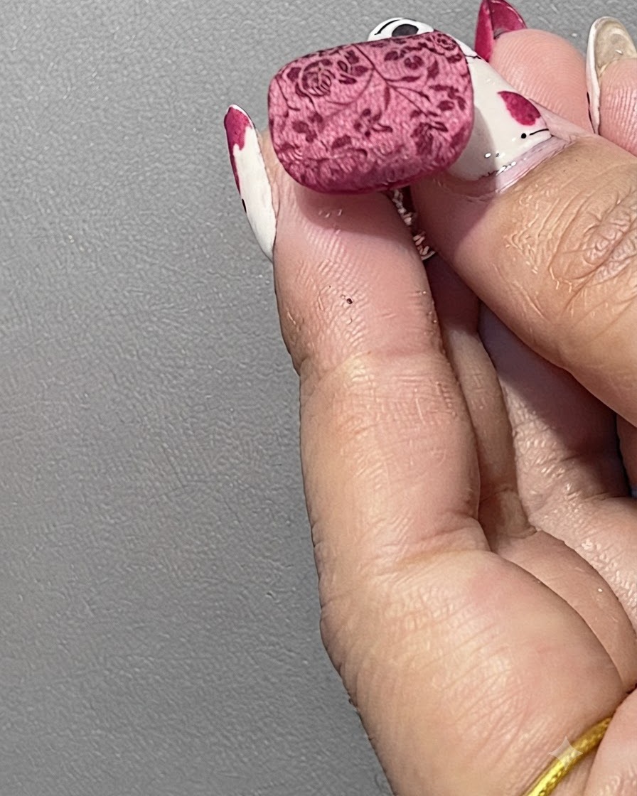 Una uña arreglada posicionada bajo una luz de curado para fijar el diseño floral cubierto de polvo.