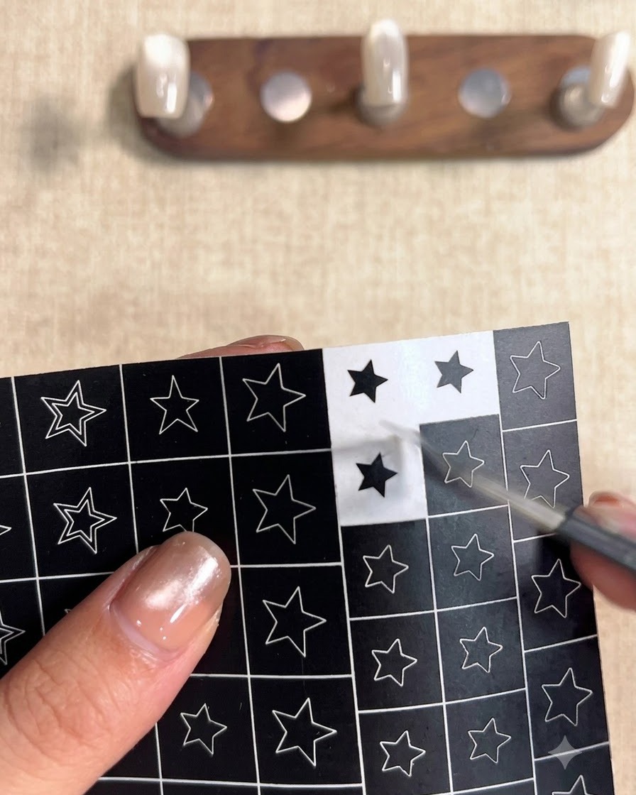 Una mano usando pinzas para despegar una pegatina cuadrada negra con un recorte de estrella hueca de una hoja de diseños de estrellas.