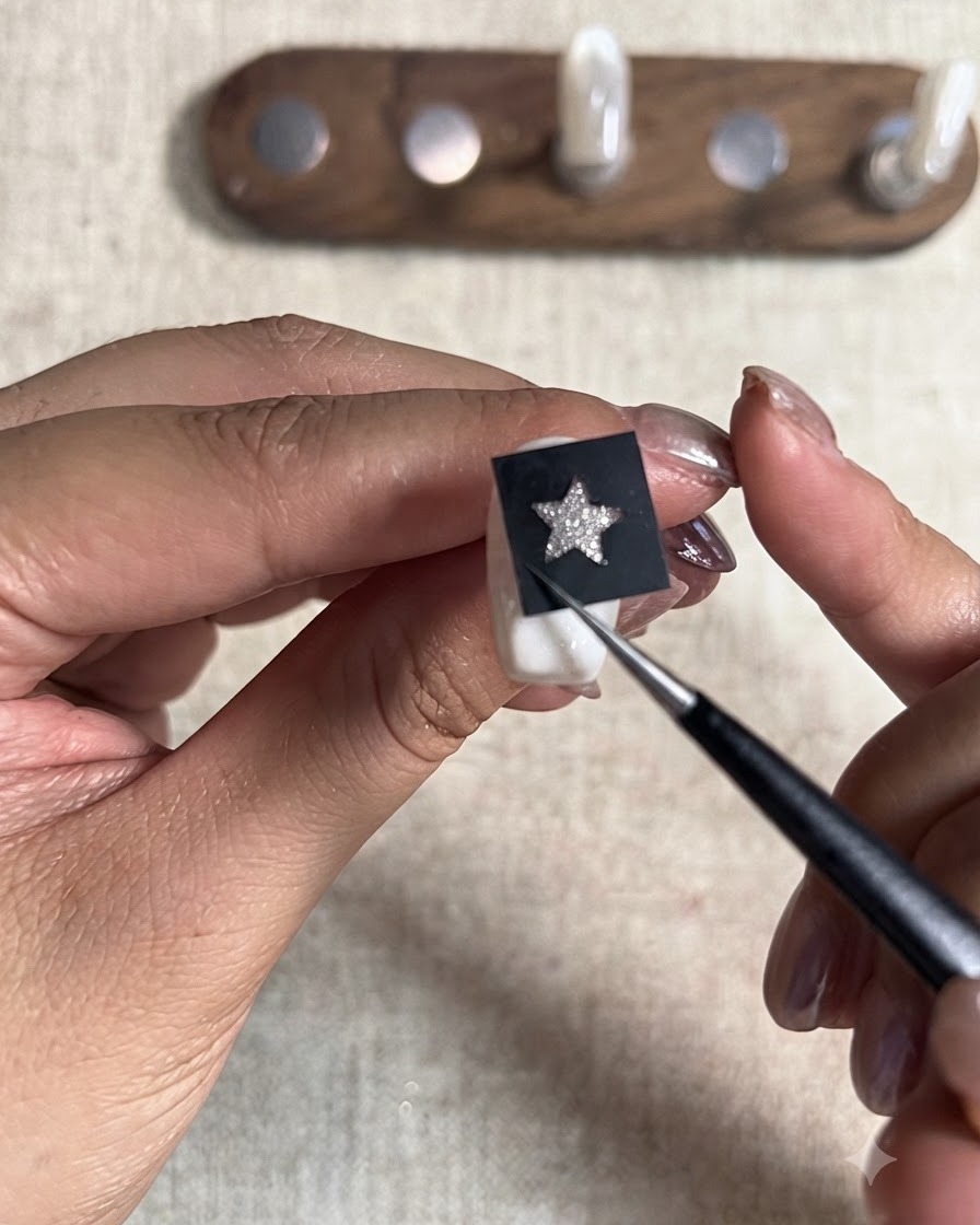 Una herramienta puntiaguda presionando firmemente una pegatina de plantilla de estrella negra colocada sobre un tip de uña pintado.
