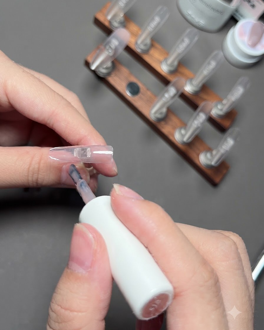 Un pincel aplicando gel de color nude en la uña del dedo anular.