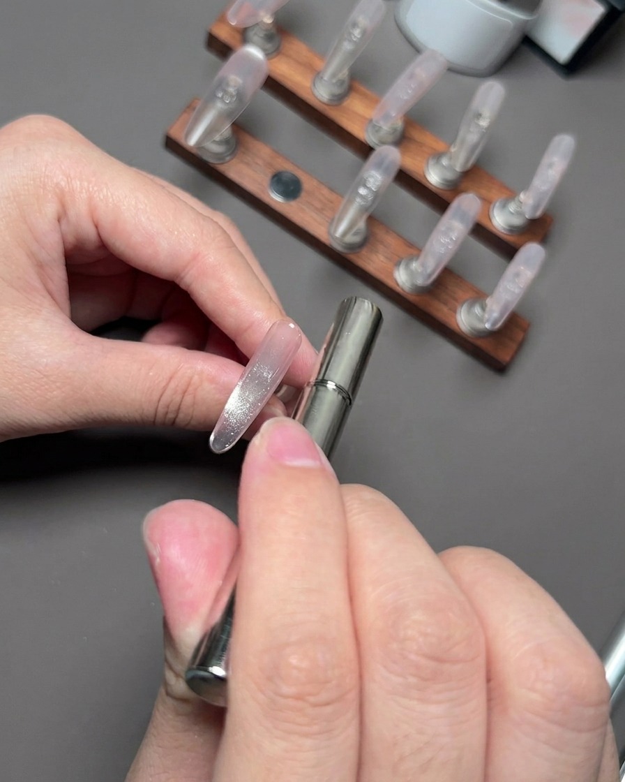 Una varita magnética flotando cerca de una uña para juntar y moldear las partículas reflectantes cat eye.