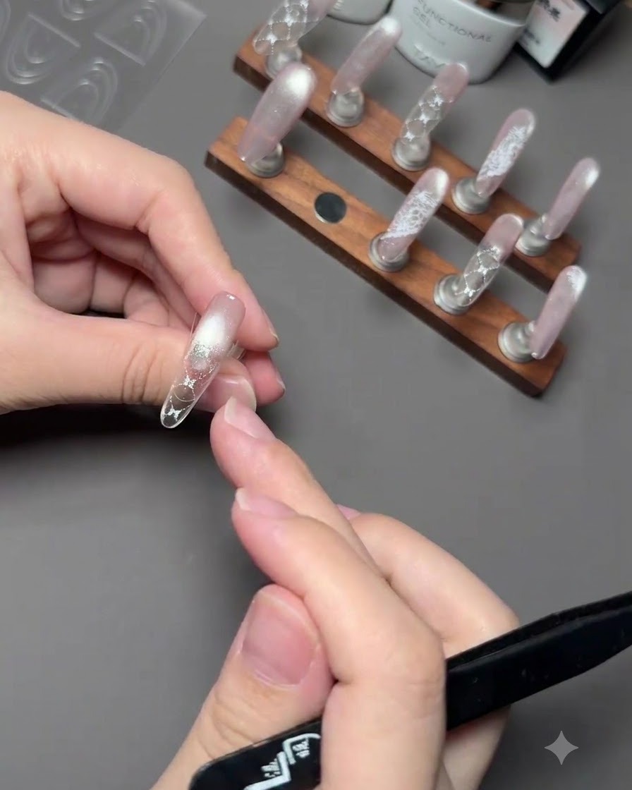 Una mano sosteniendo un pincel para aplicar esmalte en gel rosa en la punta de una uña por encima de una pegatina guía.
