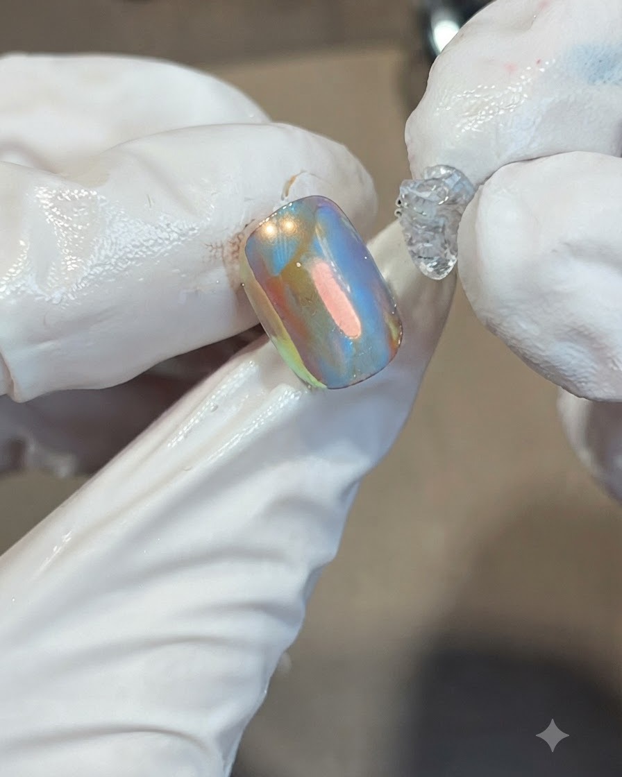 Colocando una gota de gel de caramelo suave transparente y espeso en el centro de una uña naranja y azul iridiscente.