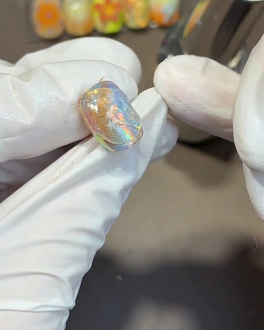 Usando una herramienta de metal para presionar texturas fluidas y onduladas en el gel transparente espeso sobre la punta de una uña iridiscente.