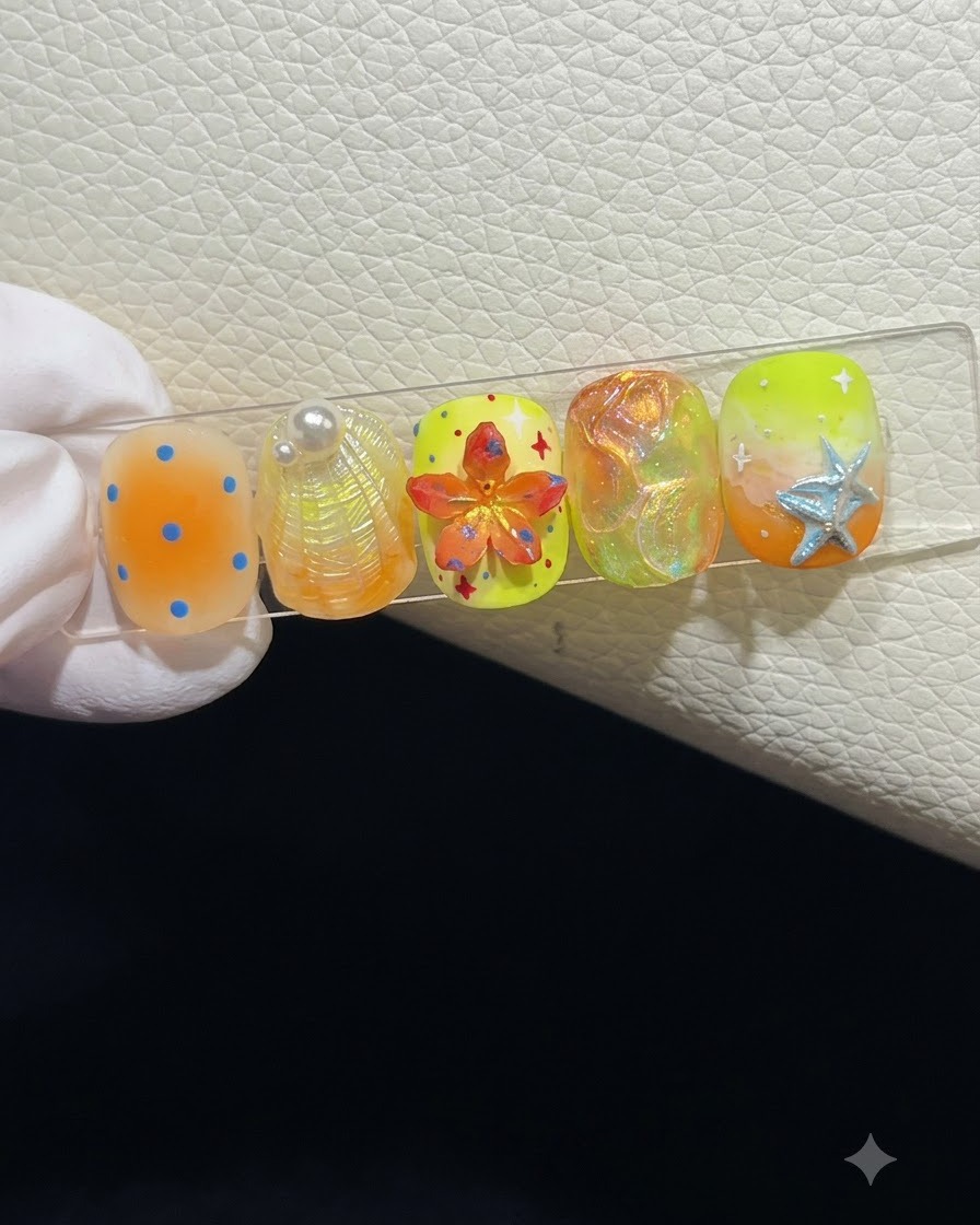 Un primer plano de un soporte de exhibición de uñas que muestra cinco uñas postizas de temática veraniega con varias texturas y arte 3D.