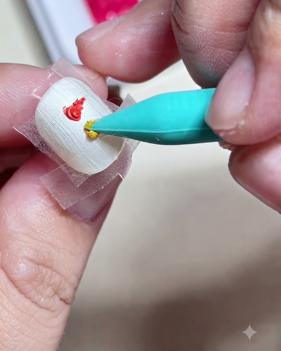 Un primer plano de una herramienta de uñas de silicona aplicando una gota de pintura de gel amarilla justo debajo de una gota roja dentro de un cuadrado con cinta en una uña.