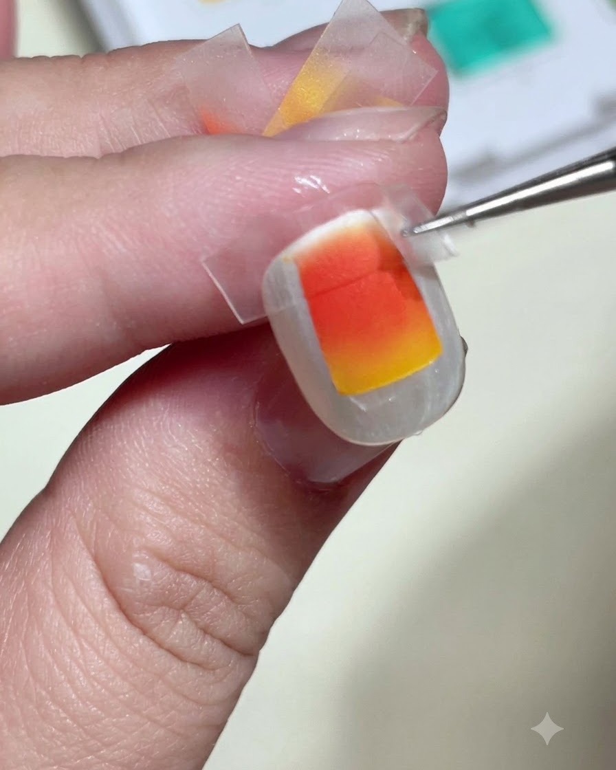 Pinzas despegando con cuidado la cinta transparente de una uña para revelar un cuadrado de degradado naranja y amarillo perfectamente nítido.