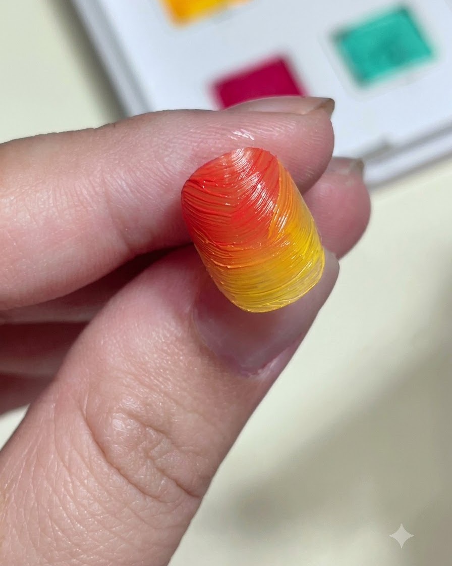 Un aplicador de esponja frotando polvo aurora brillante sobre un tip de uña con degradado naranja y amarillo texturizado.