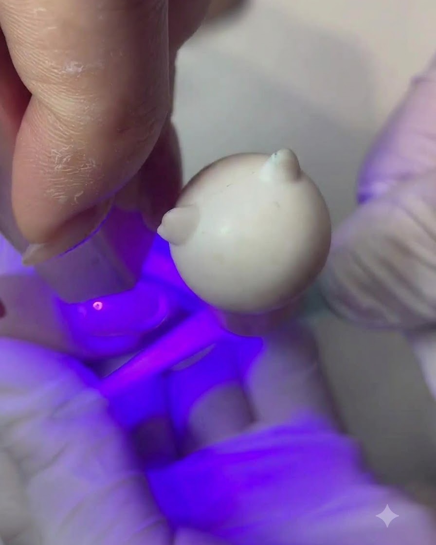 Un pincel fino aplicando una fina capa de gel color melocotón nude en una uña.