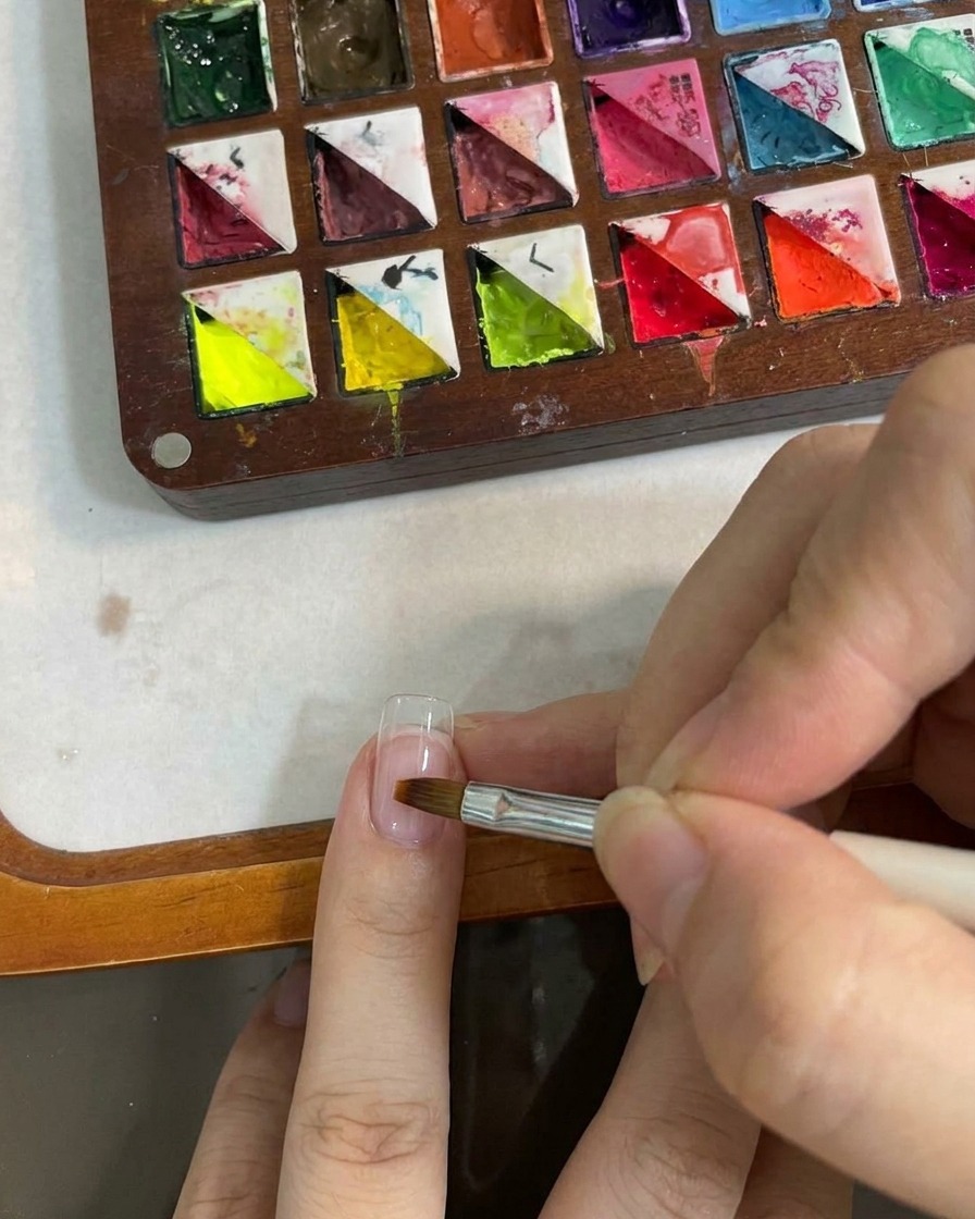Una herramienta de pincel plano difuminando el color degradado en la superficie de la uña.