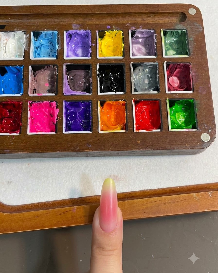 Primer plano de una uña con un degradado rosa y amarillo curándose bajo una lámpara de uñas.