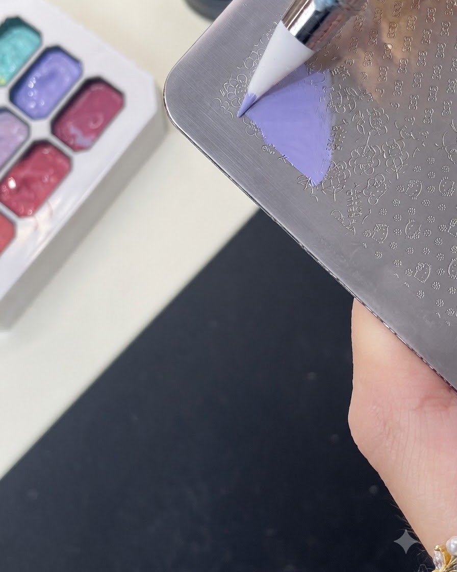 Un pincel aplicando gel de color morado sobre un patrón grabado de Hello Kitty en una placa de metal.