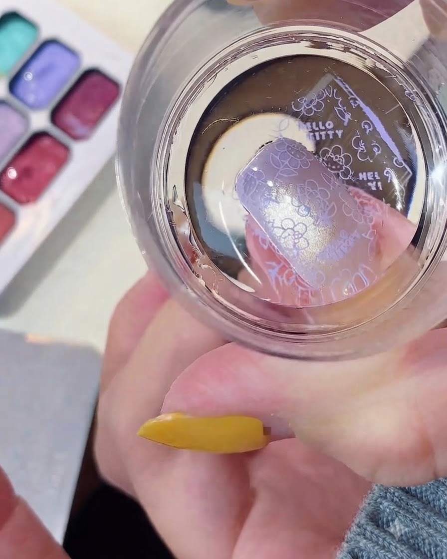Un sello de silicona transparente transfiriendo un patrón de Hello Kitty morado a una uña arreglada.