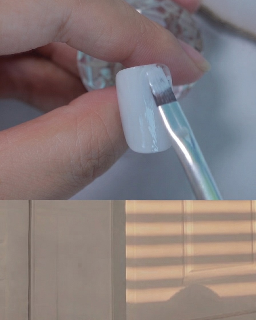 Un pincel de gel plano aplicando una capa suave de esmalte en gel gris claro sobre una uña de muestra.