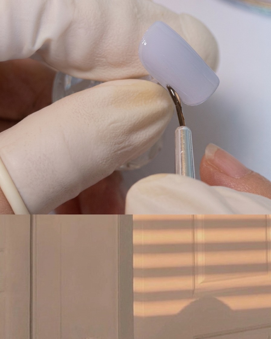 Un pincel delineador fino aplicando gel adhesivo espeso alrededor del borde de una uña gris mate.