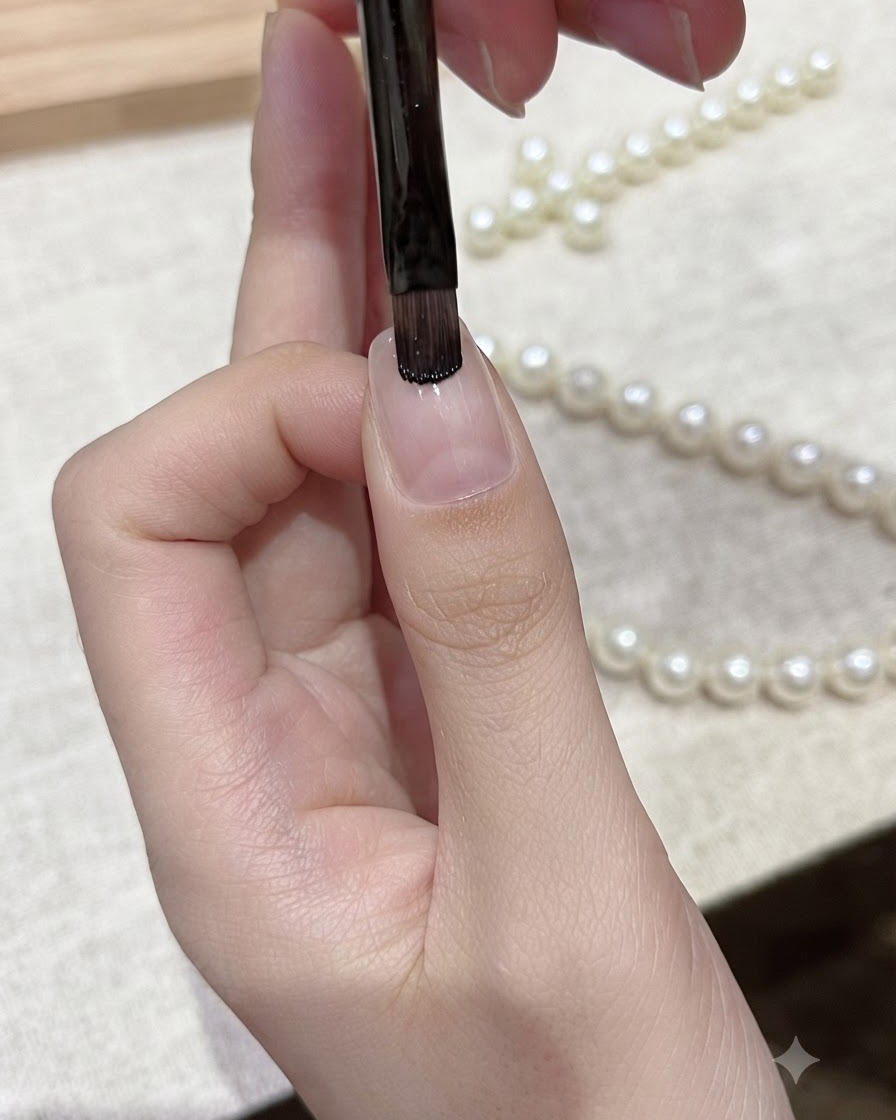 Un pincel plano de gel aplicando esmalte en gel negro directamente sobre el borde libre de una uña natural.