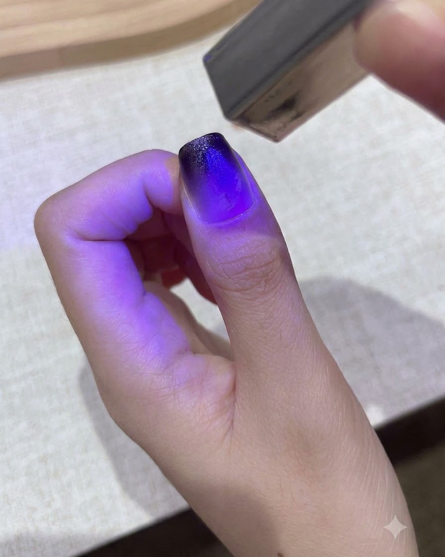 Una pequeña lámpara UV/LED morada de mano curando un diseño de gel degradado en un pulgar.