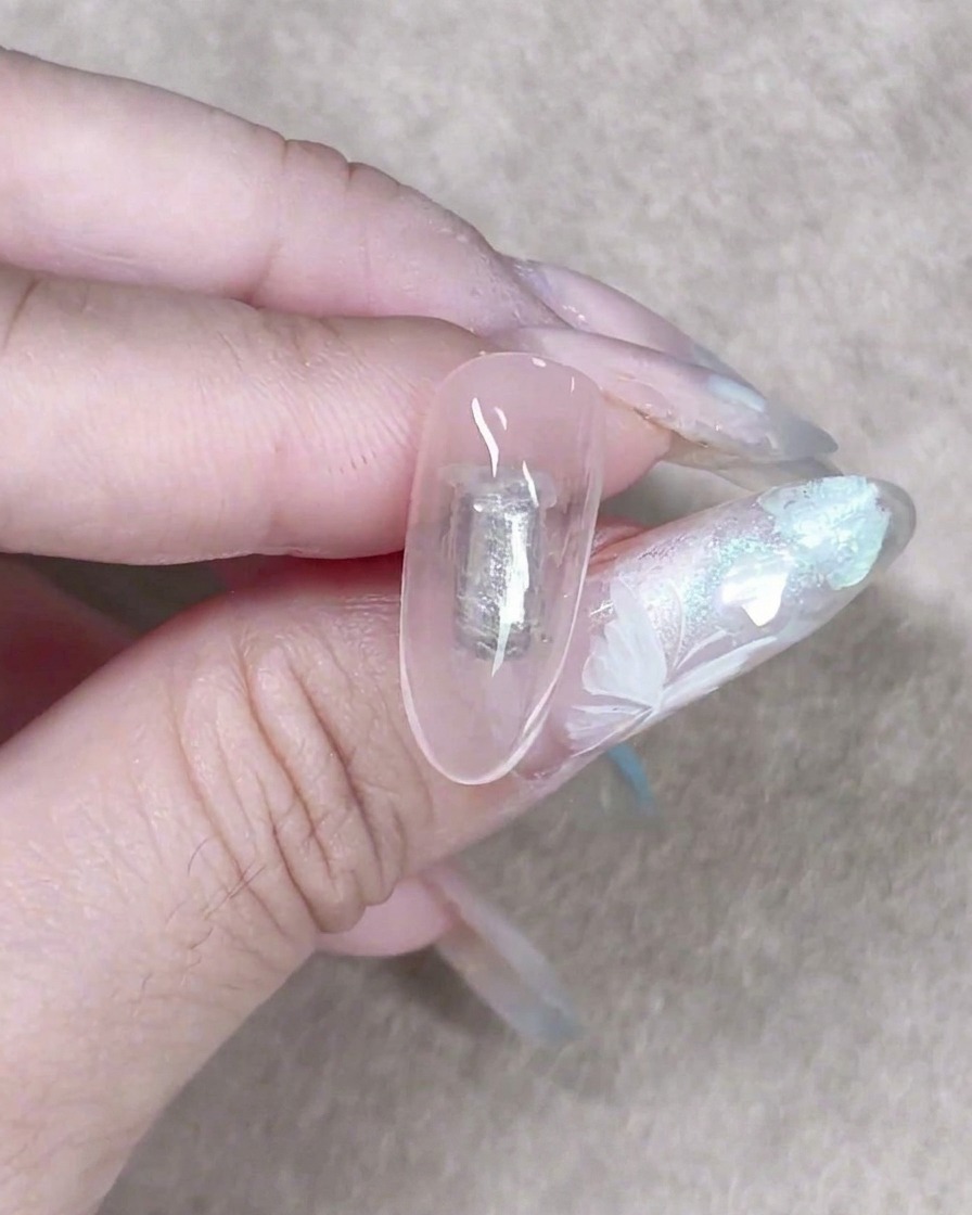 Una pequeña esponja de maquillaje dando toques suaves con un gel lechoso translúcido sobre una uña para crear un fondo suave y texturizado.