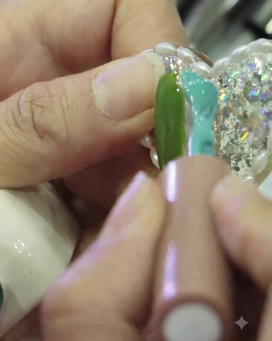 Primer plano de un pincel aplicando esmalte en gel turquesa en el lado derecho de la uña, con el lado izquierdo pintado de verde, dejando una estrecha franja sin pintar en el centro.