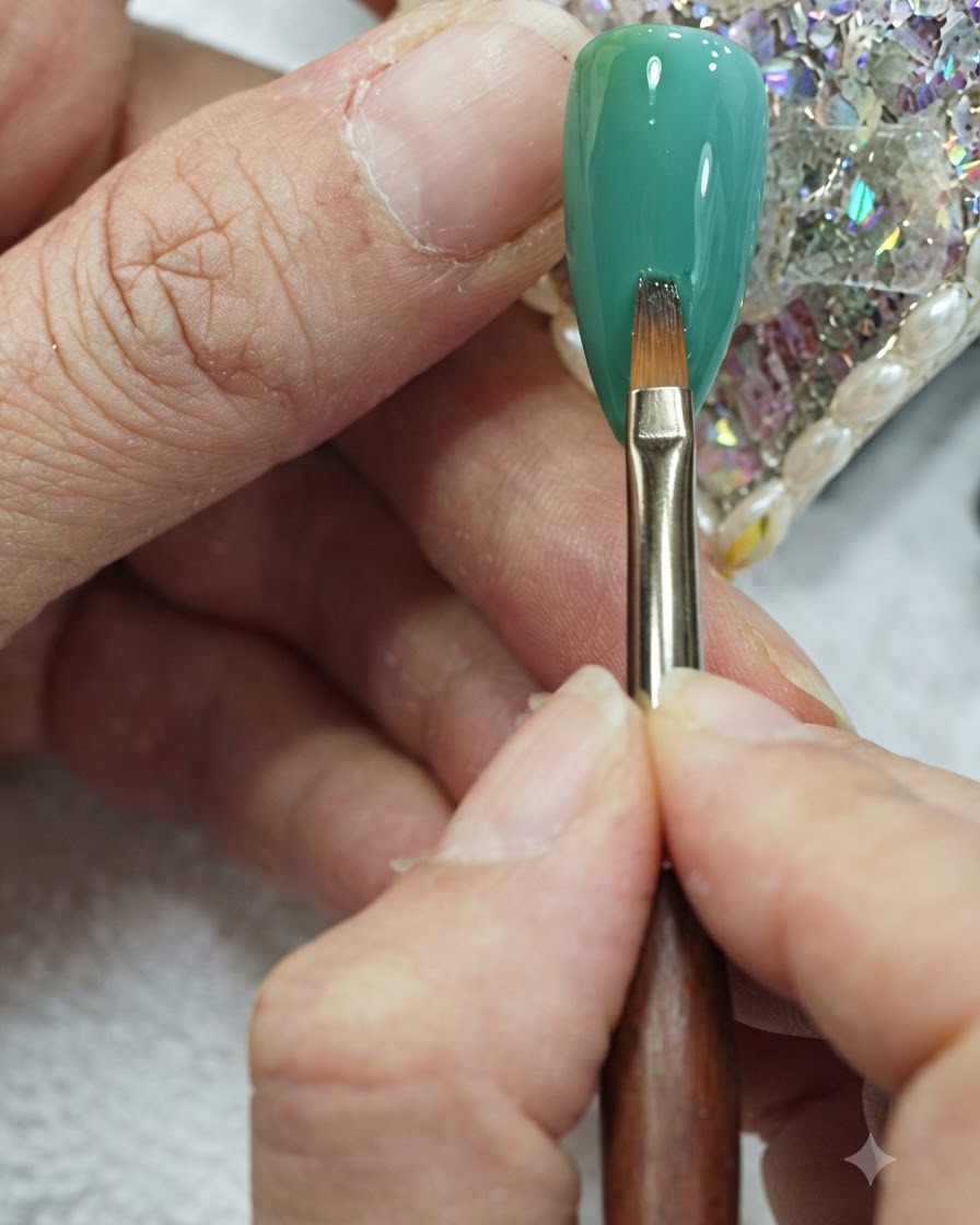 Un pincel plano para nail art realizando suaves trazos verticales en el centro de una uña con degradado verde y turquesa.