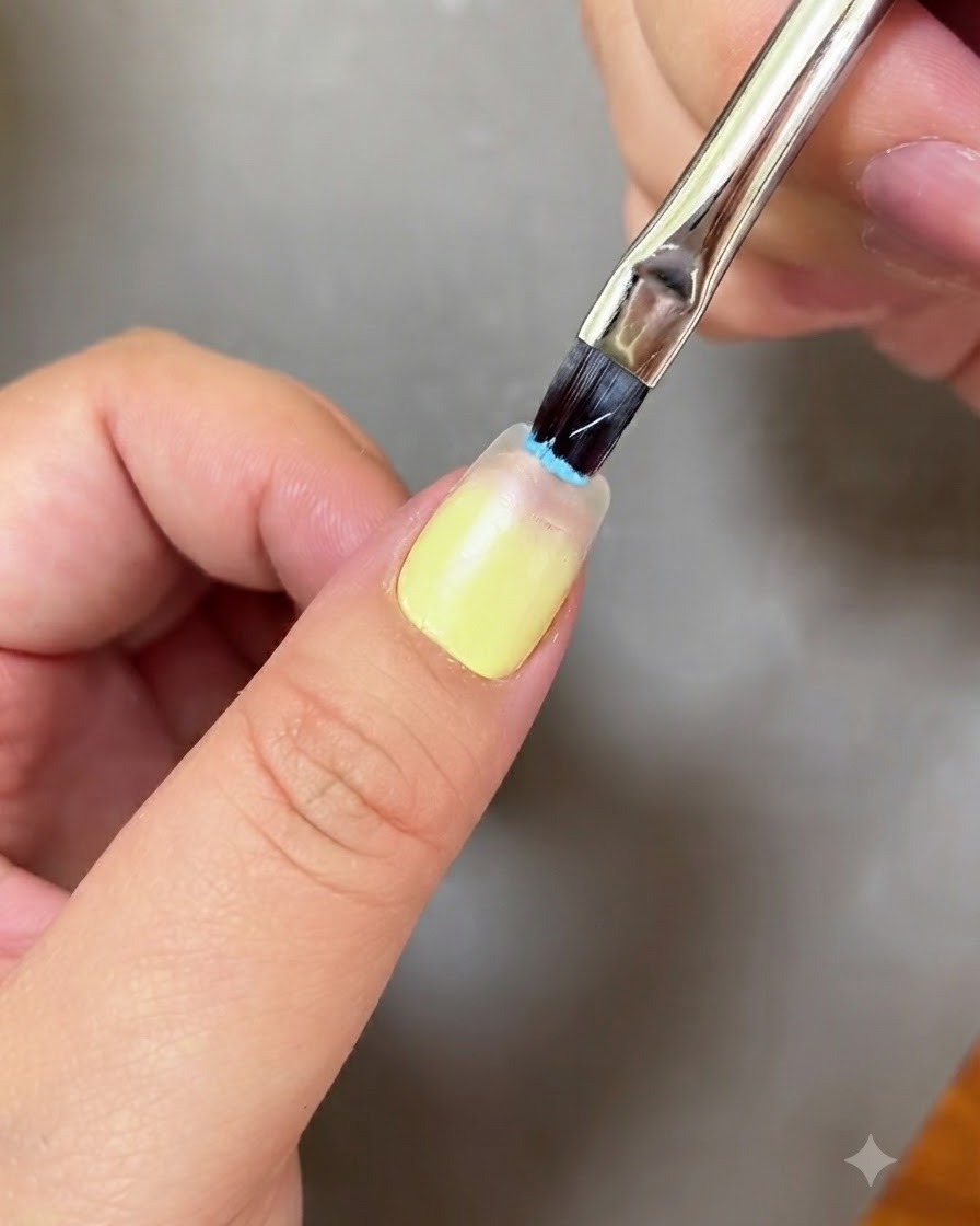 Un pincel de uñas aplicando gel azul claro en la punta de una uña.