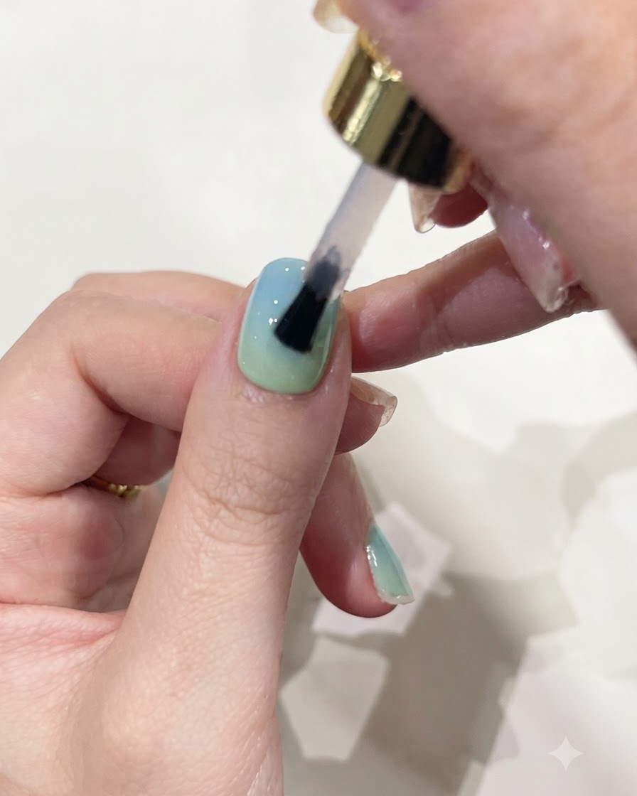 Un pincel aplicando gel constructor transparente sobre una uña con color en degradado.
