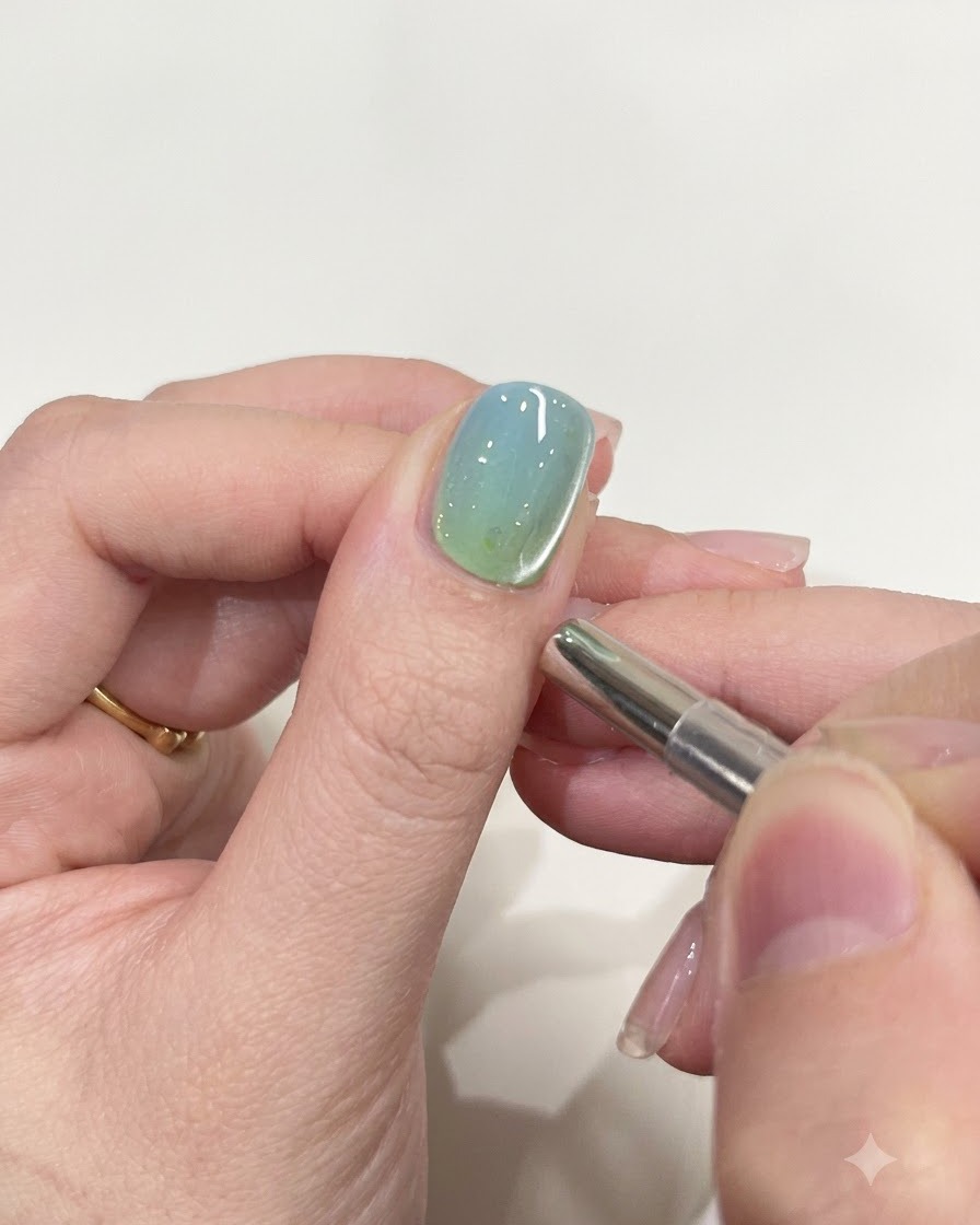 Una pequeña herramienta magnética cilíndrica flotando cerca del borde de una uña pintada con gel brillante.