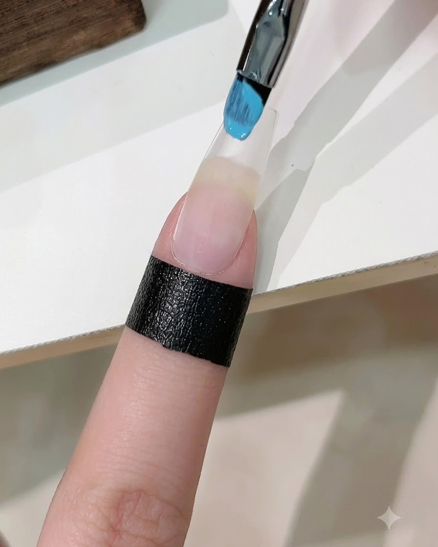 Una esponja con esmalte en gel azul y blanco aplicando un degradado sobre una uña artificial extendida.