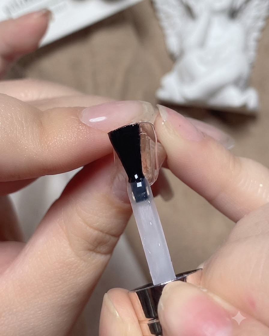 Un pincel de uñas aplicando una capa base transparente sobre una uña de práctica.
