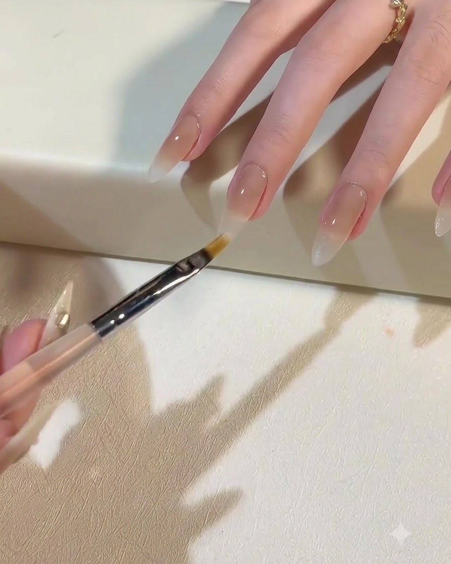 Un pincel aplicando gel blanco lechoso para crear un degradado ombré hacia la base de la uña.