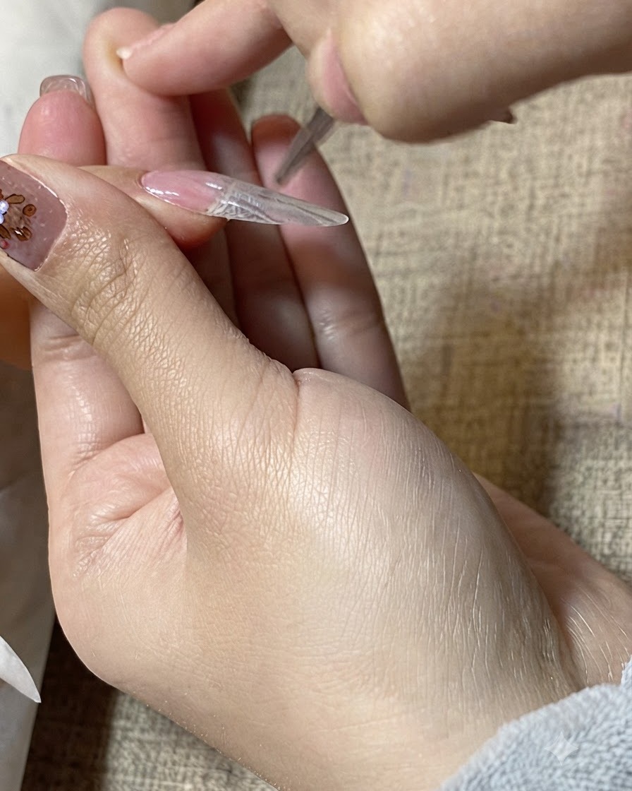Un primer plano de un pincel de detalle alisando gel transparente sobre la superficie de una extensión de uña.