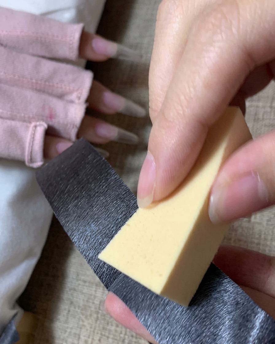 Una persona usando cinta adhesiva negra para limpiar el polvo de una esponja de maquillaje triangular de color amarillo.