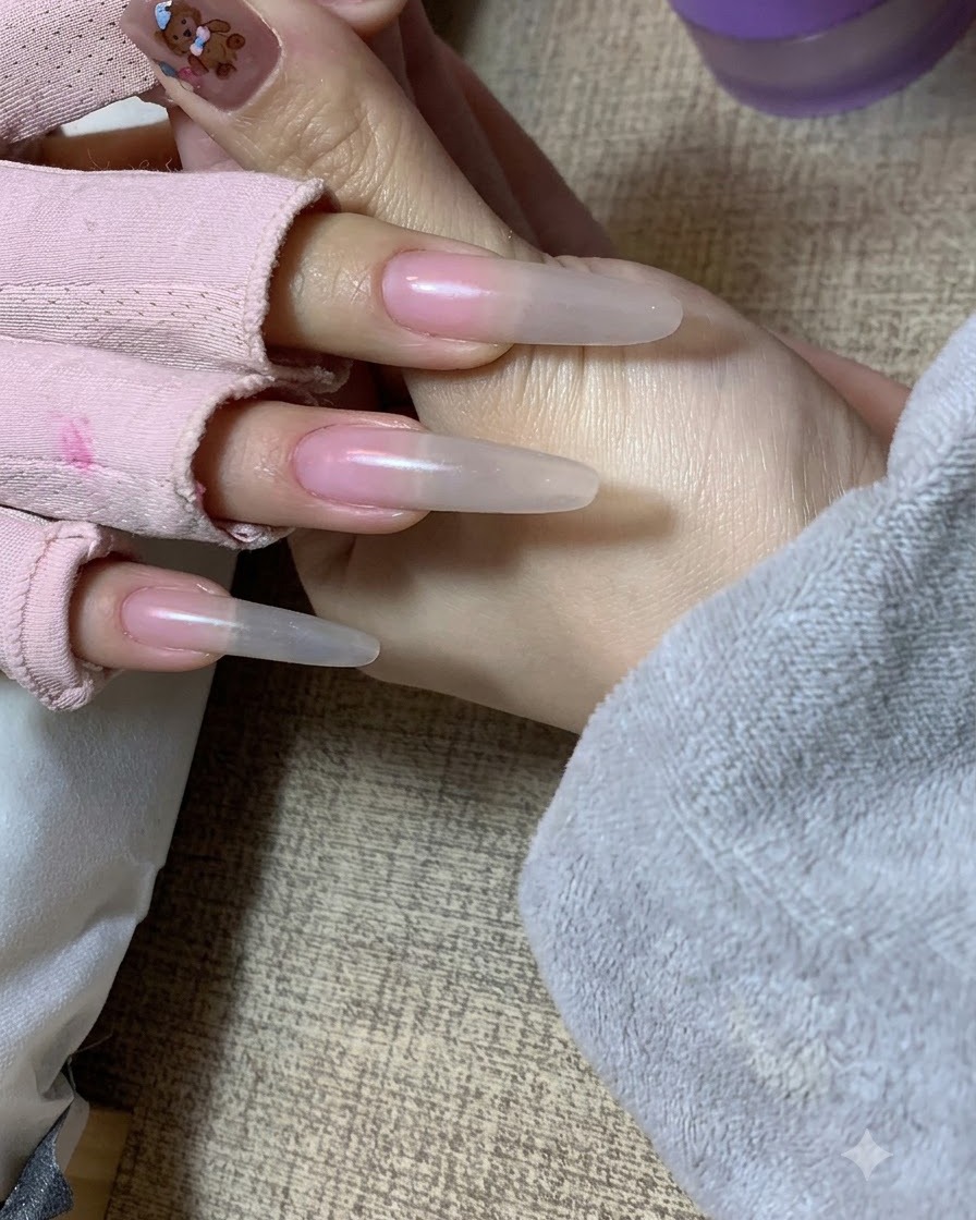 Una mano sosteniendo la mano de una clienta que muestra un efecto degradado nude suave aplicado con una esponja en las extensiones de uñas.