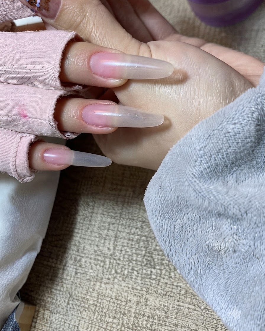 Una vista en primer plano de una mano recibiendo la segunda capa de gel nude aplicada con golpecitos cuidadosos sobre el borde libre.